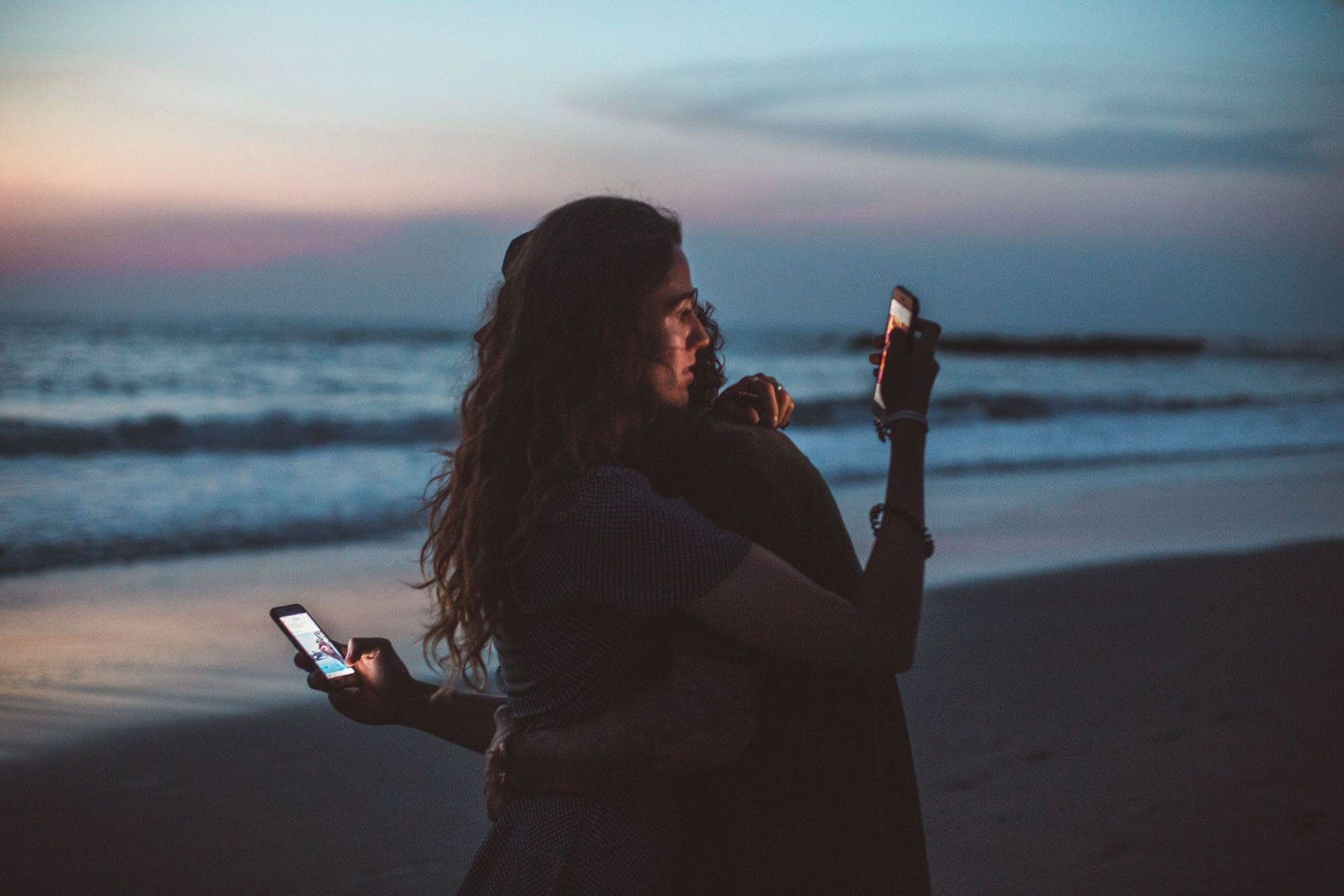 Couple hugging while using mobile phones